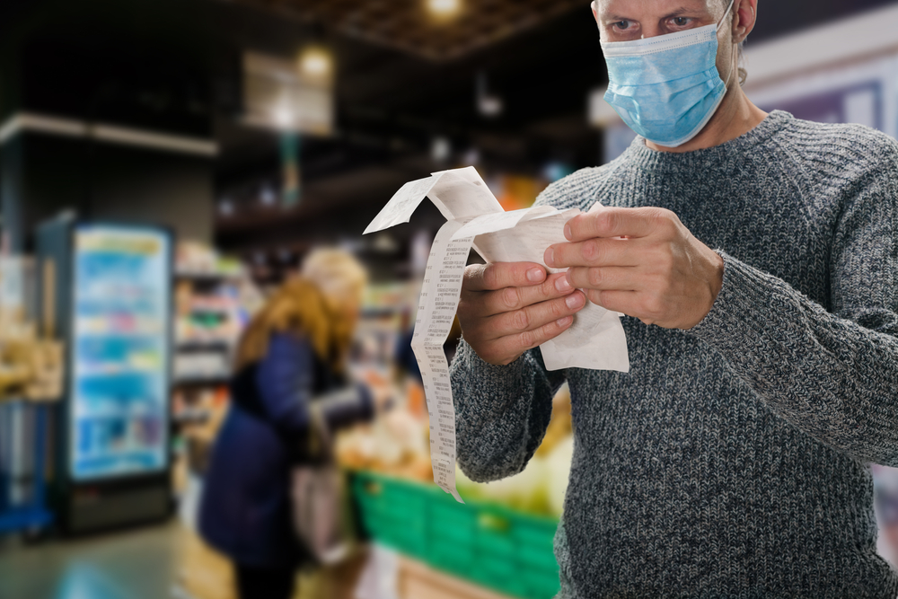 Male customer doing grocery shopping at supermarket and feeling confused by bill